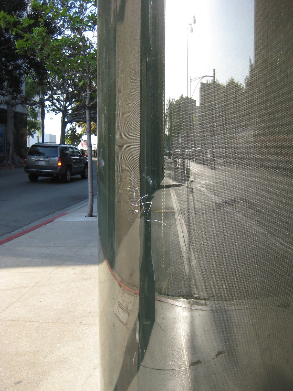 Curved storefront glass with graffiti scratched into it. Santa Monica, CA