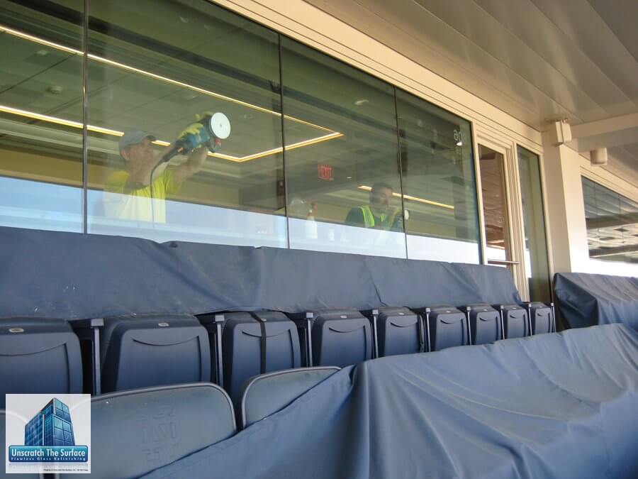 Commercial Glass Restoration Case Study: Notre Dame Stadium (2018) Richard Evans and union helper resurfacing tempered glass panels inside Notre Dame Stadium, viewed from exterior looking through glass