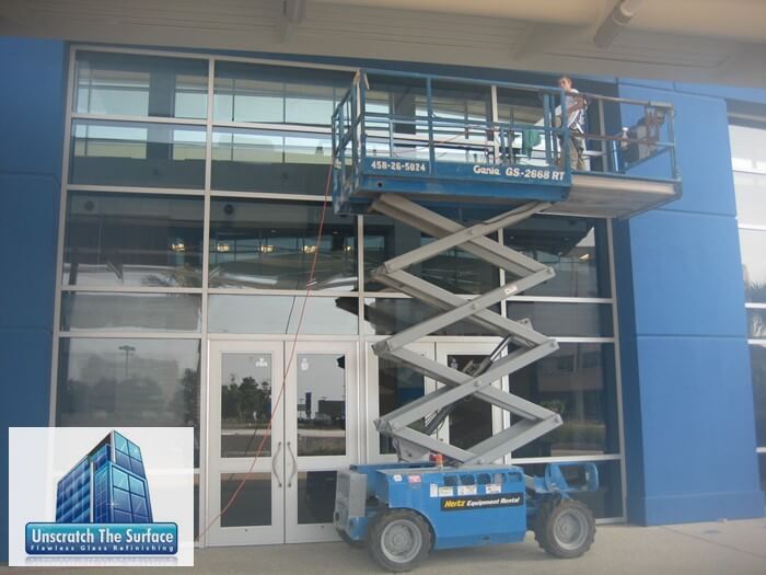 One glass scratch remover on scissor lift polishing scratches out of glass. Maximum height. Genie lift. Scratched glass project in Biloxi, MS